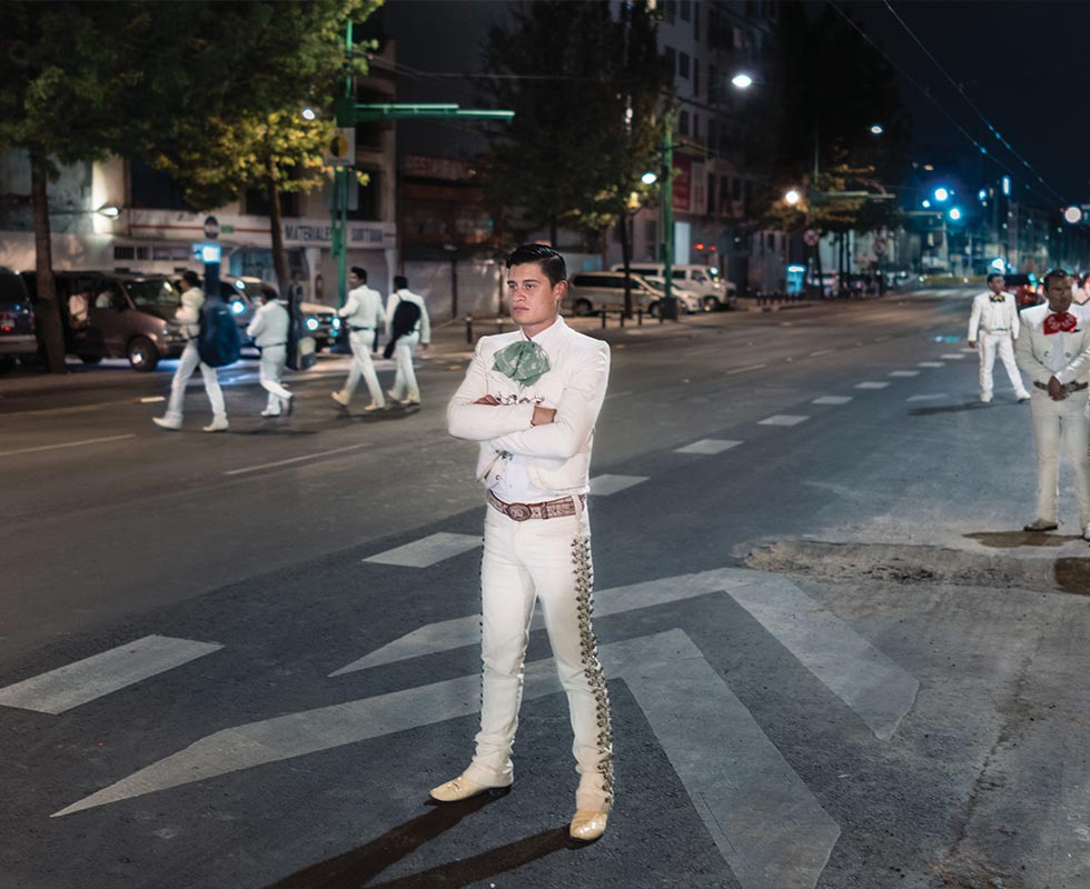 Jesus Méndez waits on the avenue beside the plaza for a car carrying customers who might want to hear a song. > Many mariachis search for customers here from 6 p.m. until 5 a.m. the next morning.